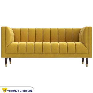 A sofa in a camel yellow color with recessed lines on the back and the base