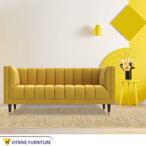 A sofa in a camel yellow color with recessed lines on the back and the base