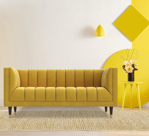 A sofa in a camel yellow color with recessed lines on the back and the base