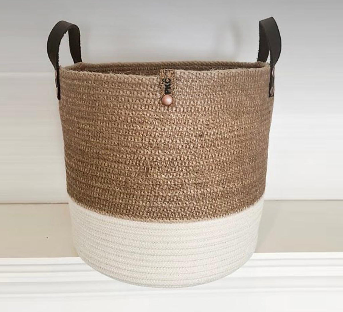 Round jute basket with a light-colored base and leather handles